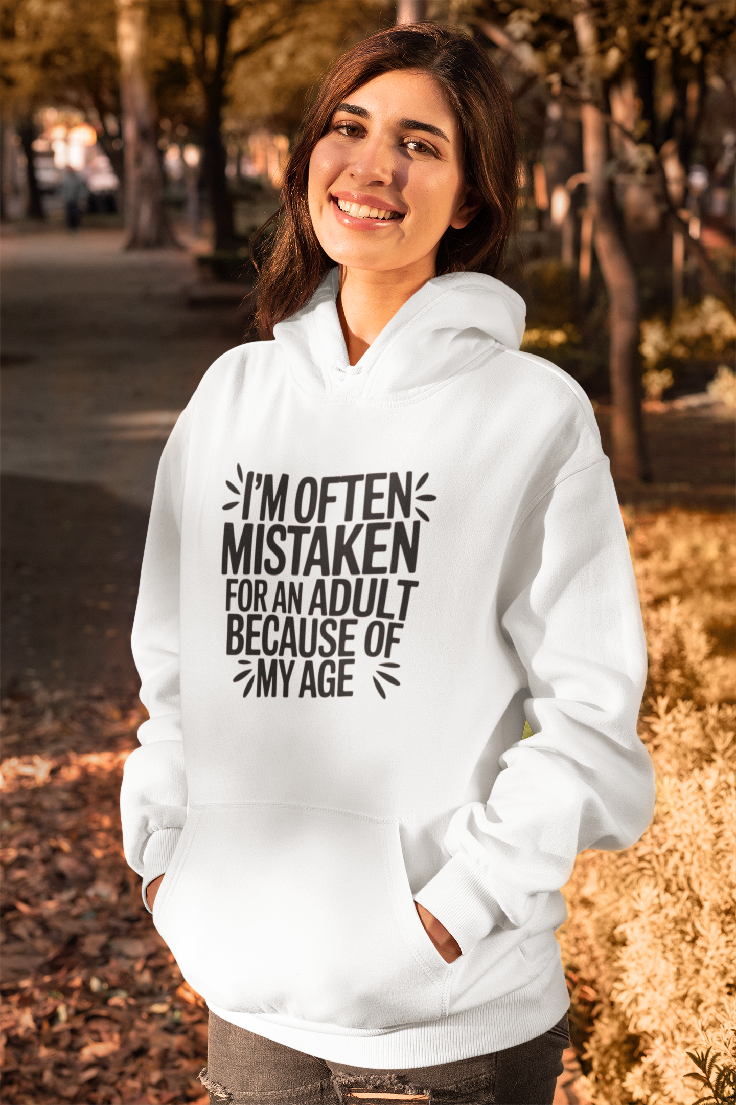 Unisex hoodie with ‘I’m Often Mistaken for an Adult’ text, soft fleece interior, light neutral color.