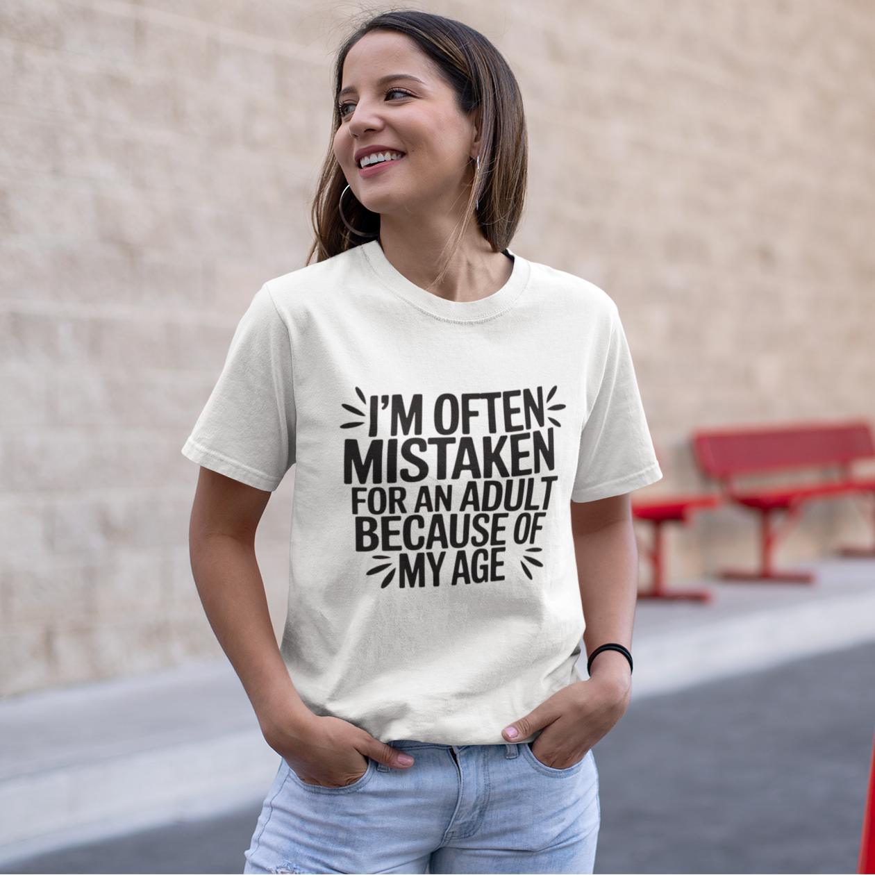 Woman wearing a t-shirt that says "I'm often mistaken for an adult because of my age" standing outdoors near a building.